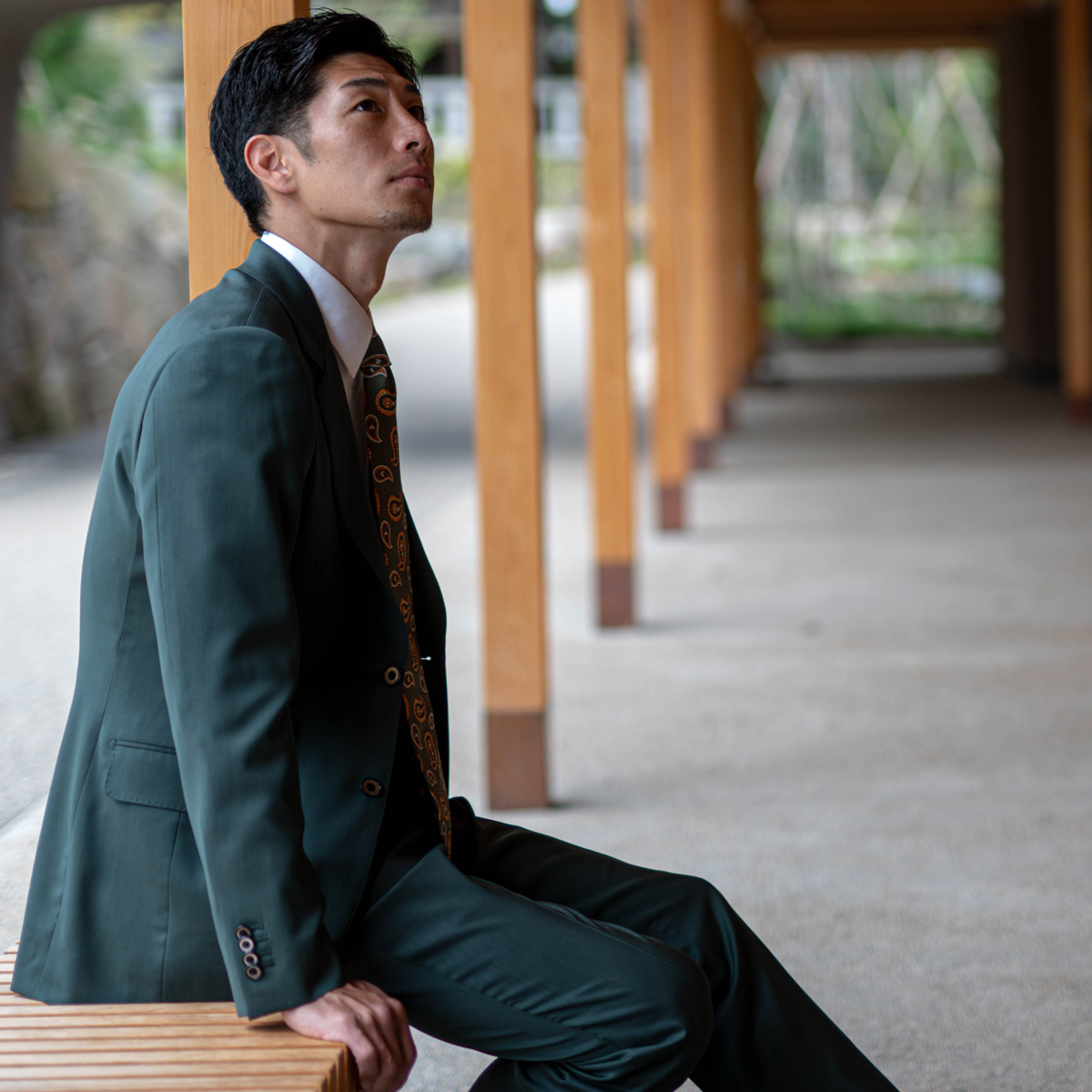 木の柱が並ぶ回廊を歩く、緑系のジャケットを着た男性の後ろ姿